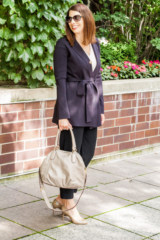 woman wearing blue coat, casual clothes, and holding a bag