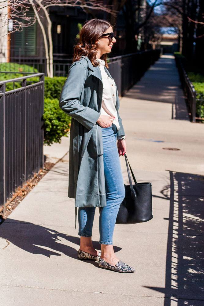 woman with hands in her pocket and wearing a coat, jeans, and flat sandals