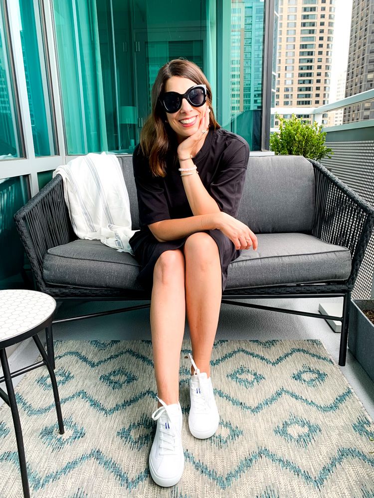 woman sitting down and wearing black dress from everlane summer essentials