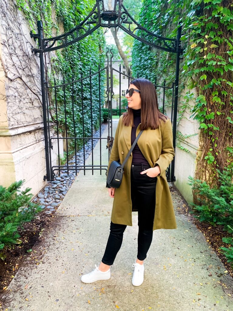 woman in black top and pants, green coat, and saddle bag