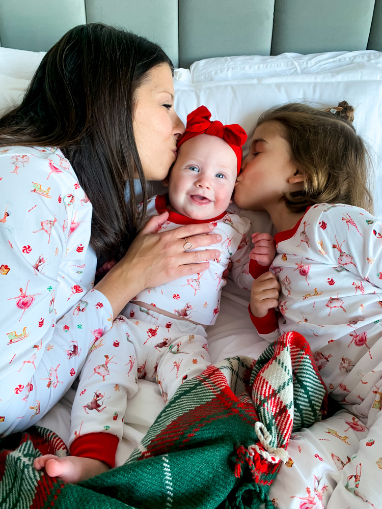 Mom and daughter kissing baby in their matching Christmas PJ's