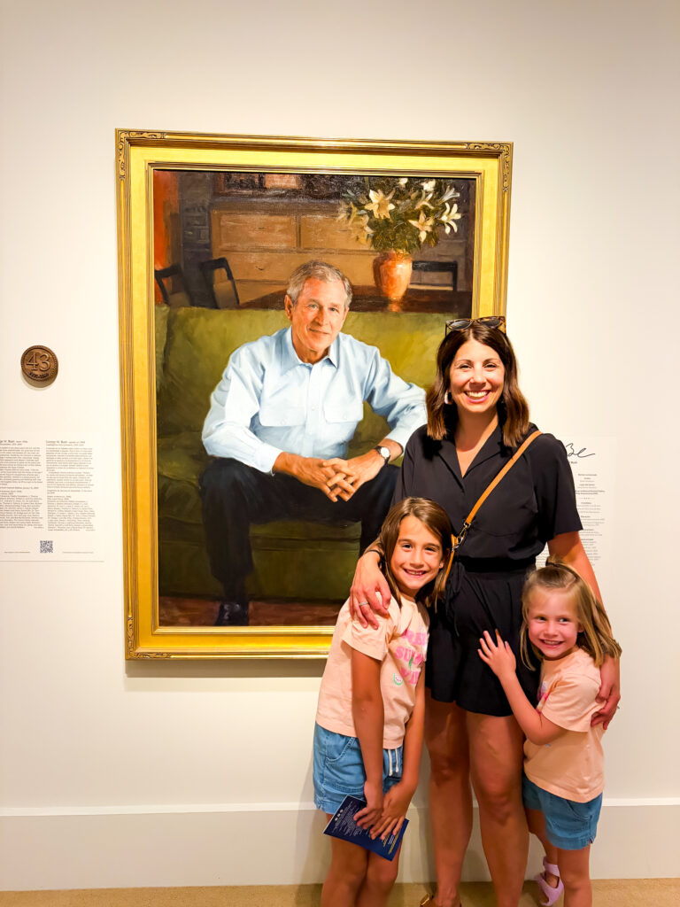 Family with two young children walking along the Portrait Gallery in Washington, DC, with George Bush in the background on a sunny day