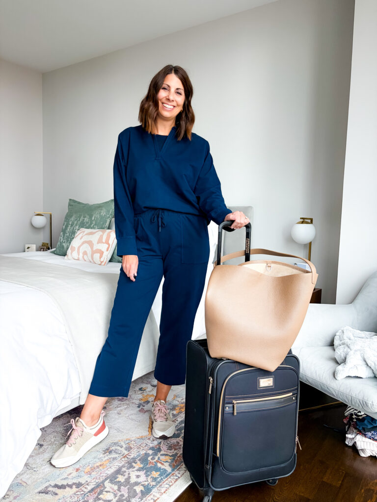 Woman over 40 in a J.Jill Elevation Knit quarter-zip and straight-leg pants carrying a weekender bag
